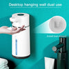A white automatic foaming soap dispenser is shown hanging on a teal wall, demonstrating its dual use.
