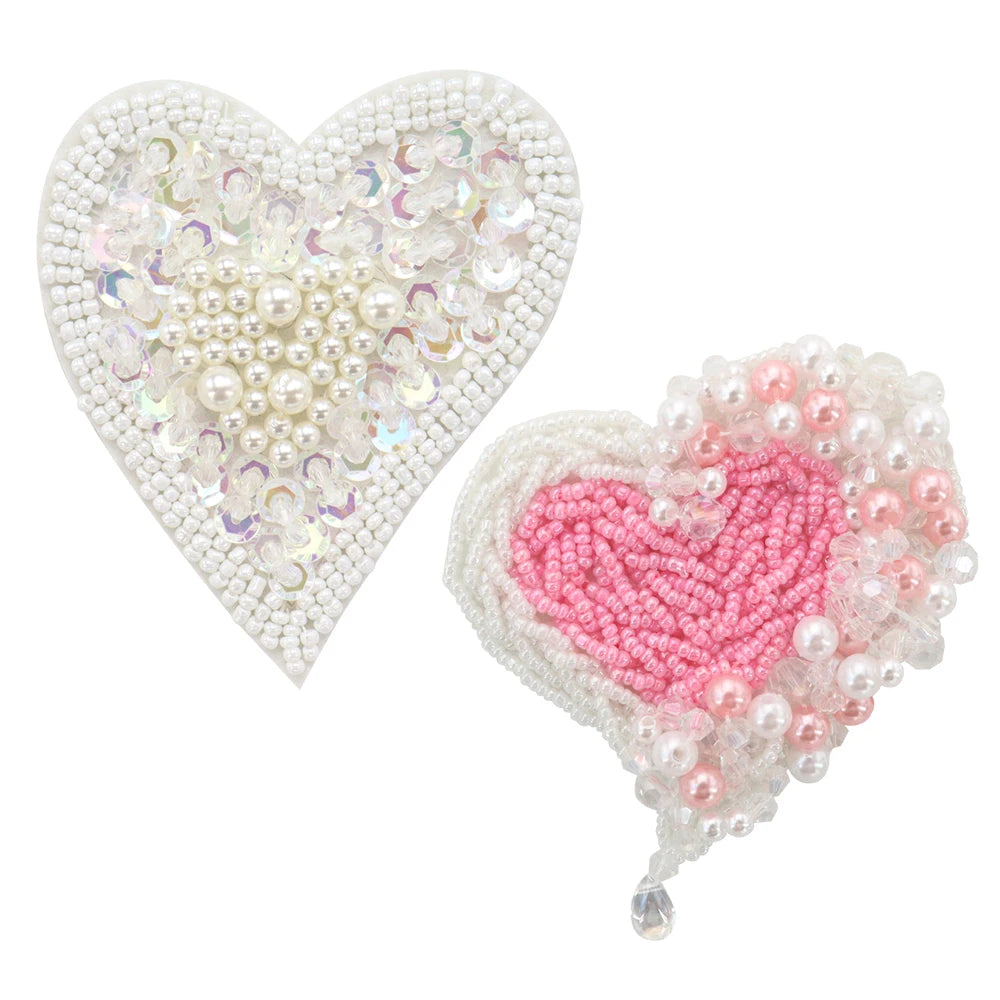 A heart-shaped patch made of white and iridescent beads and rhinestones, next to a pink heart patch with pearl accents.