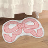 A pink bow-shaped absorbent non-slip doormat placed on a wooden floor.