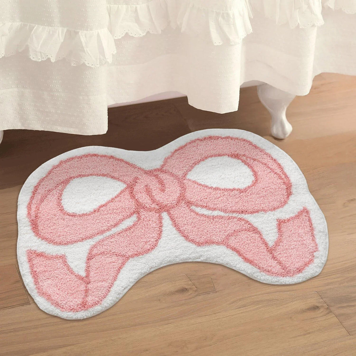 A pink bow-shaped absorbent non-slip doormat placed on a wooden floor.