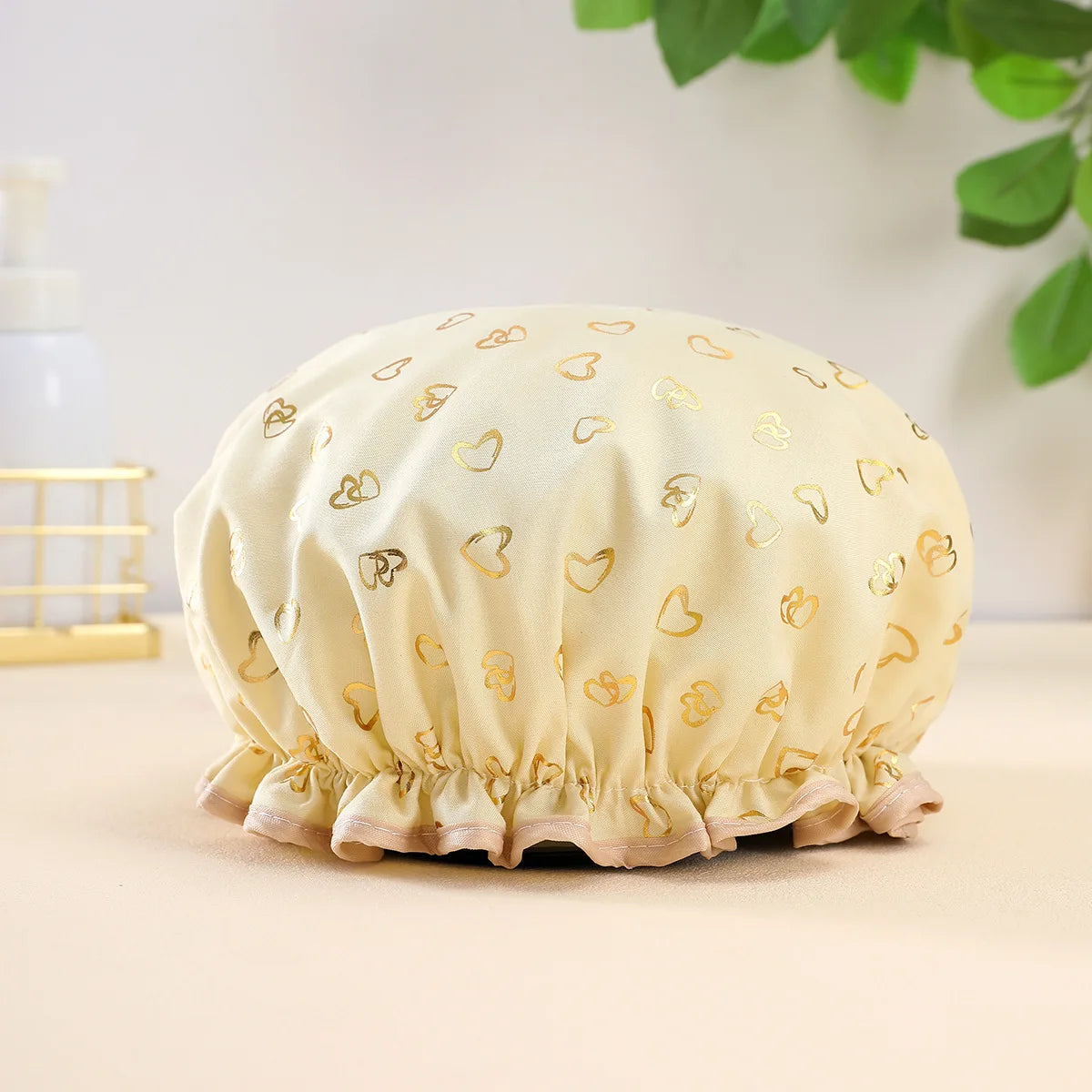 A beige reusable elastic shower cap with gold heart embroidery resting on a light surface.