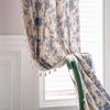 A light blue and cream floral cotton-linen curtain with tassels hanging in a window.