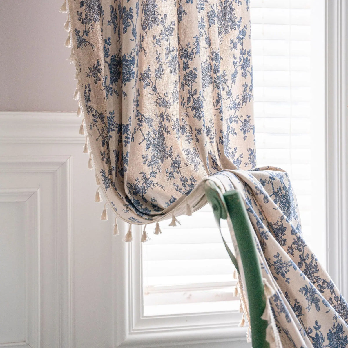 A light blue and cream floral cotton-linen curtain with tassels hanging in a window.