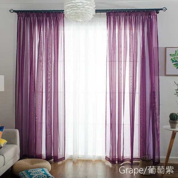 Purple sheer voile curtains with a rod pocket hanging in front of a bright window.