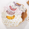 A collection of light-colored muslin cotton baby bibs and burp cloths in floral patterns with adjustable snap closures.