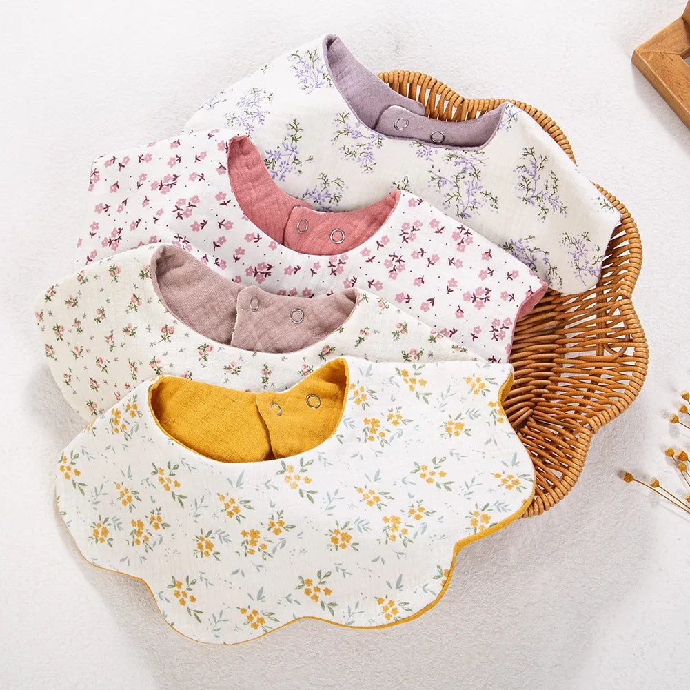 A collection of light-colored muslin cotton baby bibs and burp cloths in floral patterns with adjustable snap closures.