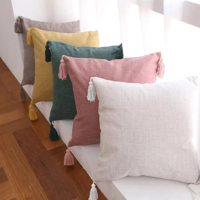 A collection of linen throw pillows in muted tones including yellow, olive green, pink, and cream with tassels.
