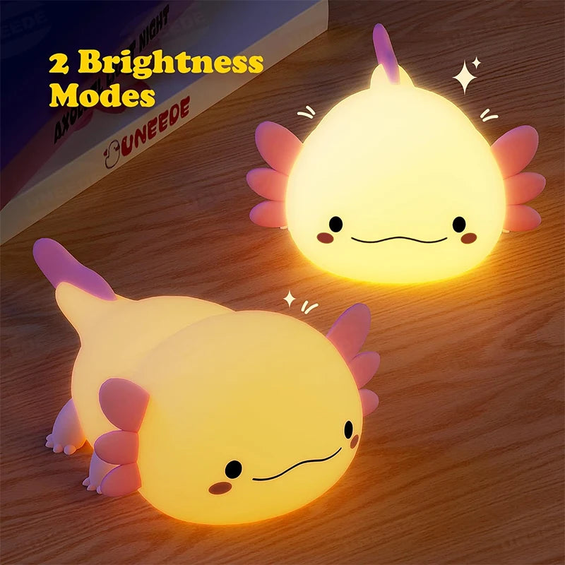 A glowing yellow axolotl night light with pink fins resting on a wooden surface.