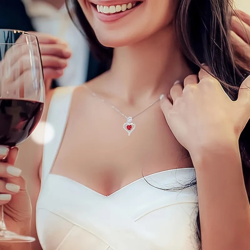 A woman wearing a white dress and a silver heart pendant necklace, holding a glass of red wine.