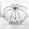 A clear, retro transparent arch umbrella with a black frame and delicate floral design resting on white bedding.