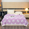 A purple throw blanket with white bow patterns is displayed on a bed against a light wood headboard.