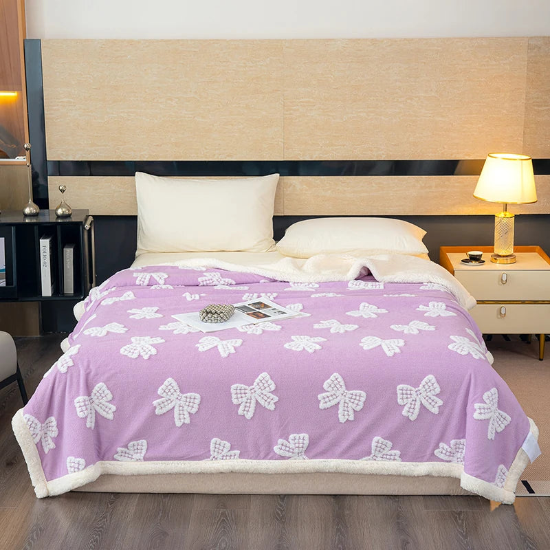 A purple throw blanket with white bow patterns is displayed on a bed against a light wood headboard.