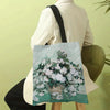 A canvas tote bag featuring a watercolor floral design of white roses and greenery, held by a person.