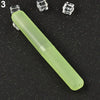A light green, elongated travel toothbrush case with a clear cap and small cube-shaped accessories is shown on a dark surface