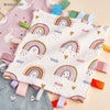 A white baby sensory tag comfort blanket with colorful rainbow patterns and clouds is shown on a light background.