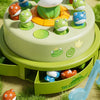A green cake decorated with plastic frog figures in various colors, set on a grassy surface.