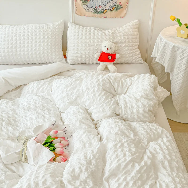 A white quilted duvet cover set with a stuffed bear and pink flowers on a bed.