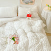 A white quilted duvet cover set with a sheep plush toy and pink flowers on a bed.