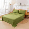 A light green bedding set with a fitted sheet, flat sheet, and pillowcases is displayed on a bed in a bright room.