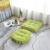 A bright lime green thick corduroy floor cushion is placed on a light gray patterned rug next to a window.
