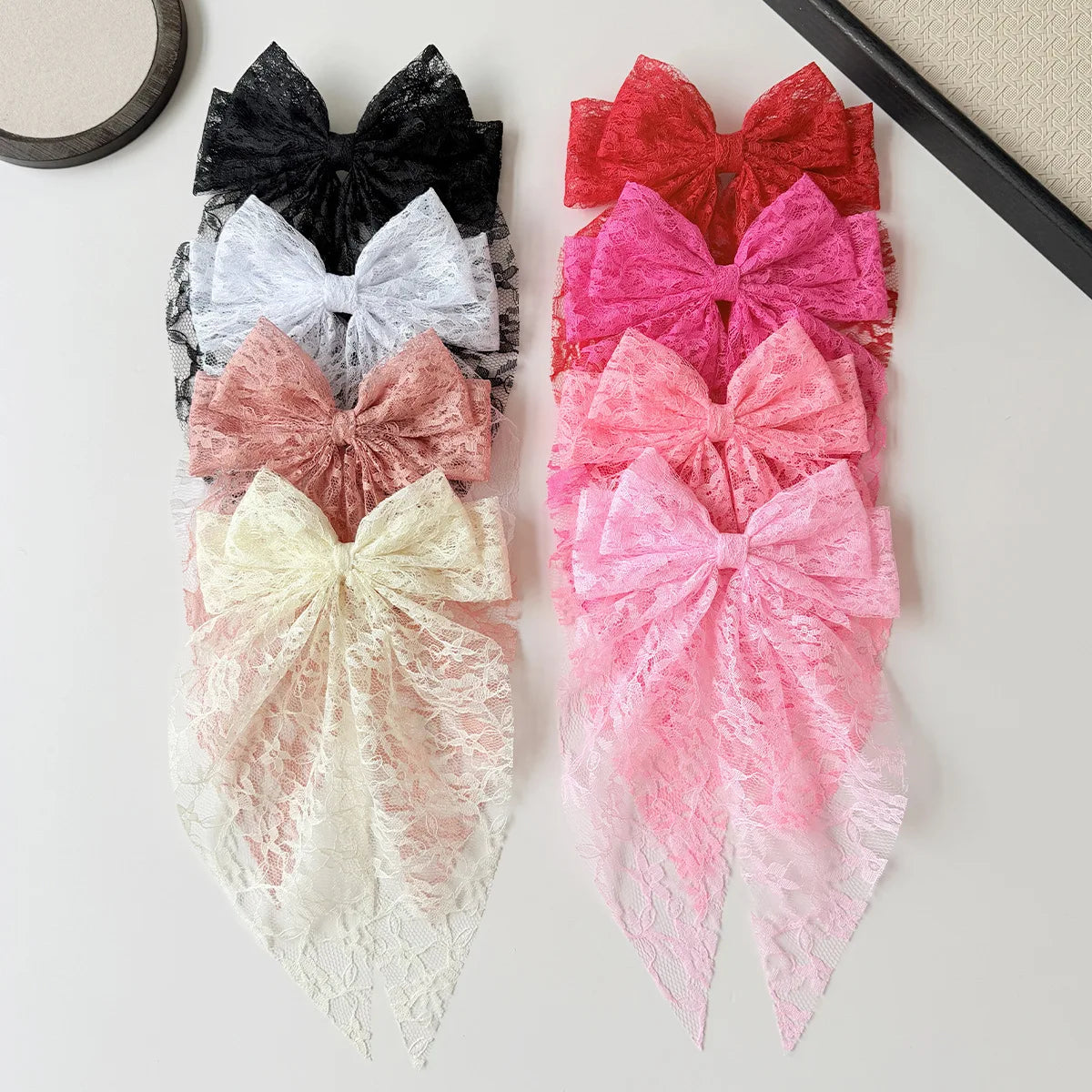 A collection of colorful lace bows in various shades including black, gray, white, pink, and red, displayed on a light surfac
