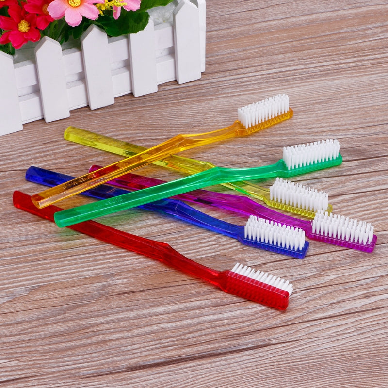 A set of six colorful hard bristled toothbrushes with white bristles arranged on a wooden surface.