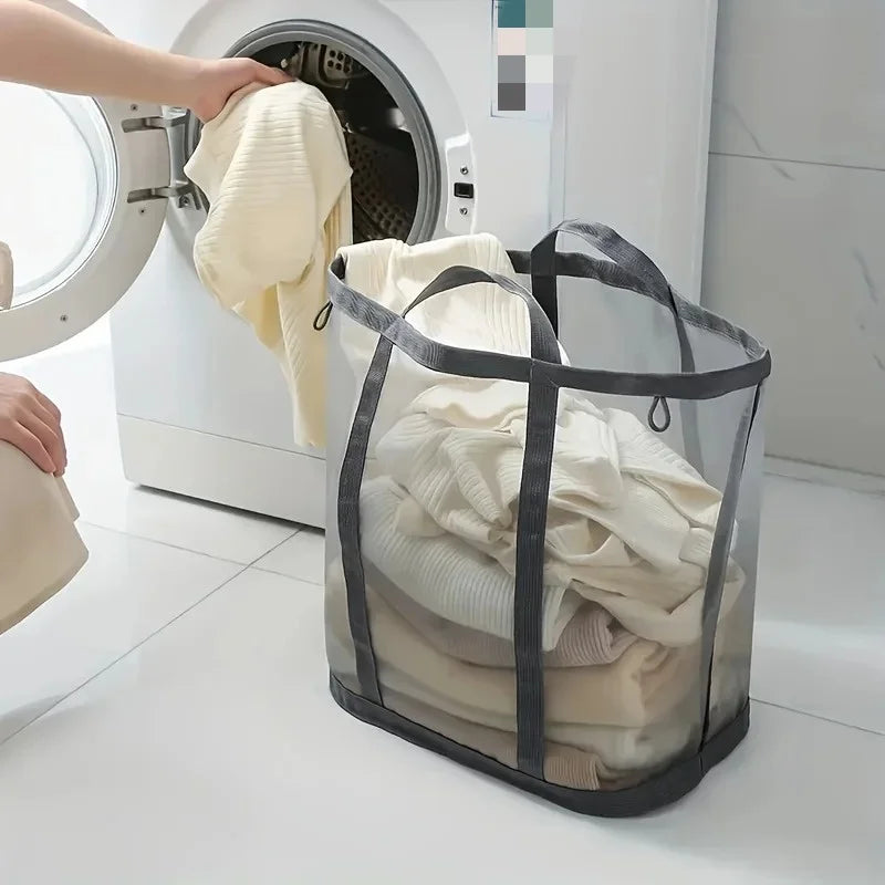 A person is placing a yellow sweater into a clear mesh laundry basket next to a white washing machine.