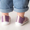 A close-up of a baby's feet wearing purple and beige breathable soft-sole shoes.