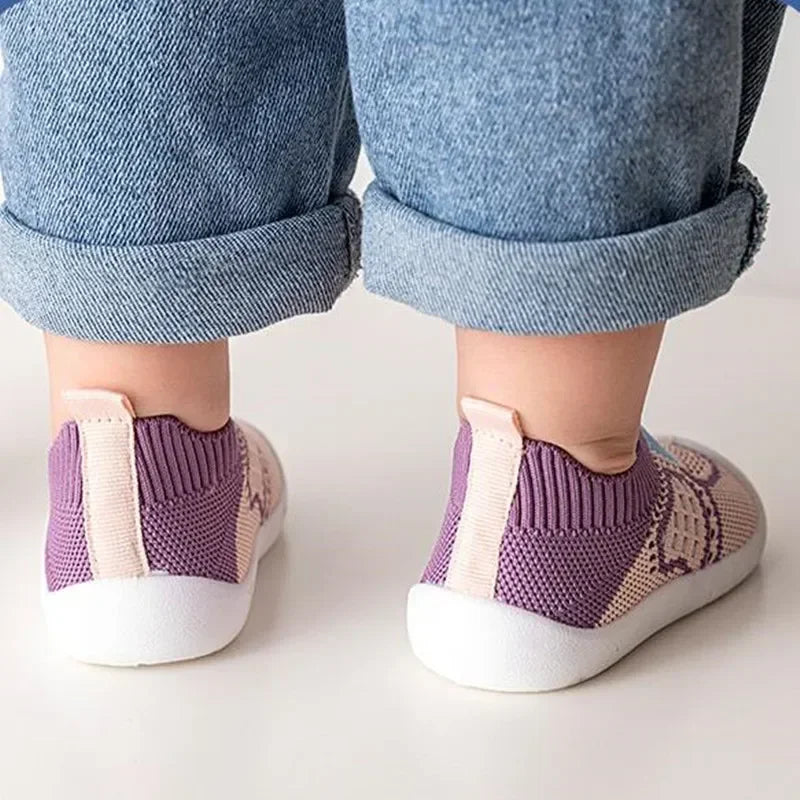A close-up of a baby's feet wearing purple and beige breathable soft-sole shoes.