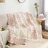 A pink and cream floral patchwork quilt draped over a sofa in a bright room.