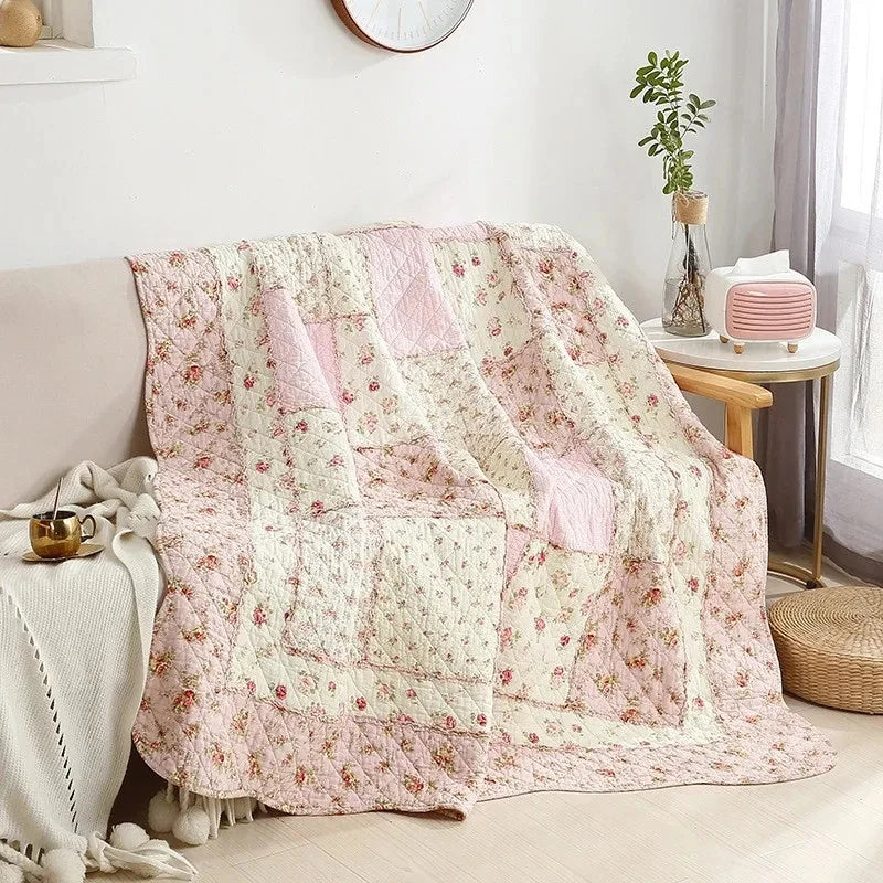 A pink and cream floral patchwork quilt draped over a sofa in a bright room.
