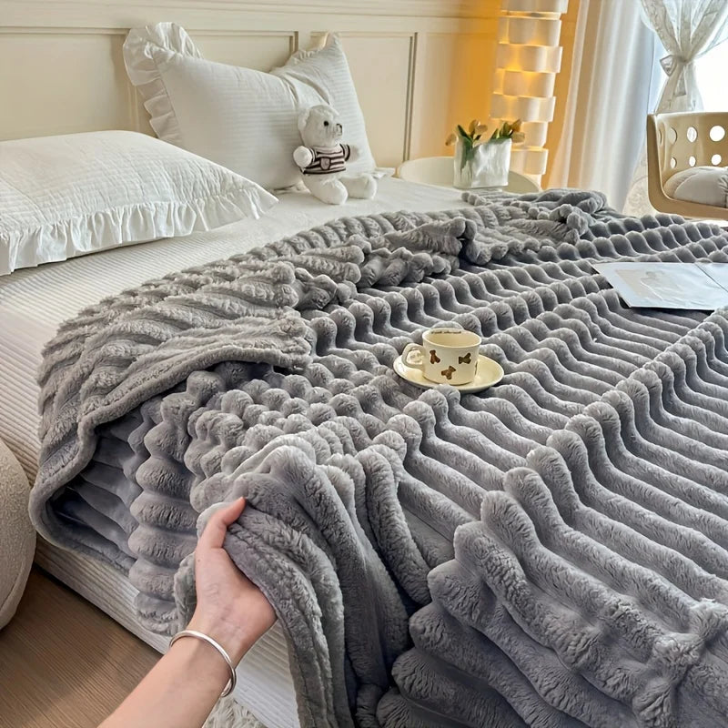 A gray fluffy flannel blanket draped over a bed, featuring a white stuffed animal and a teacup.