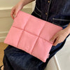Pinke gesteppte Puffer-Laptoptasche mit Reißverschluss, gehalten von Person in dunklem Jeanshemd.