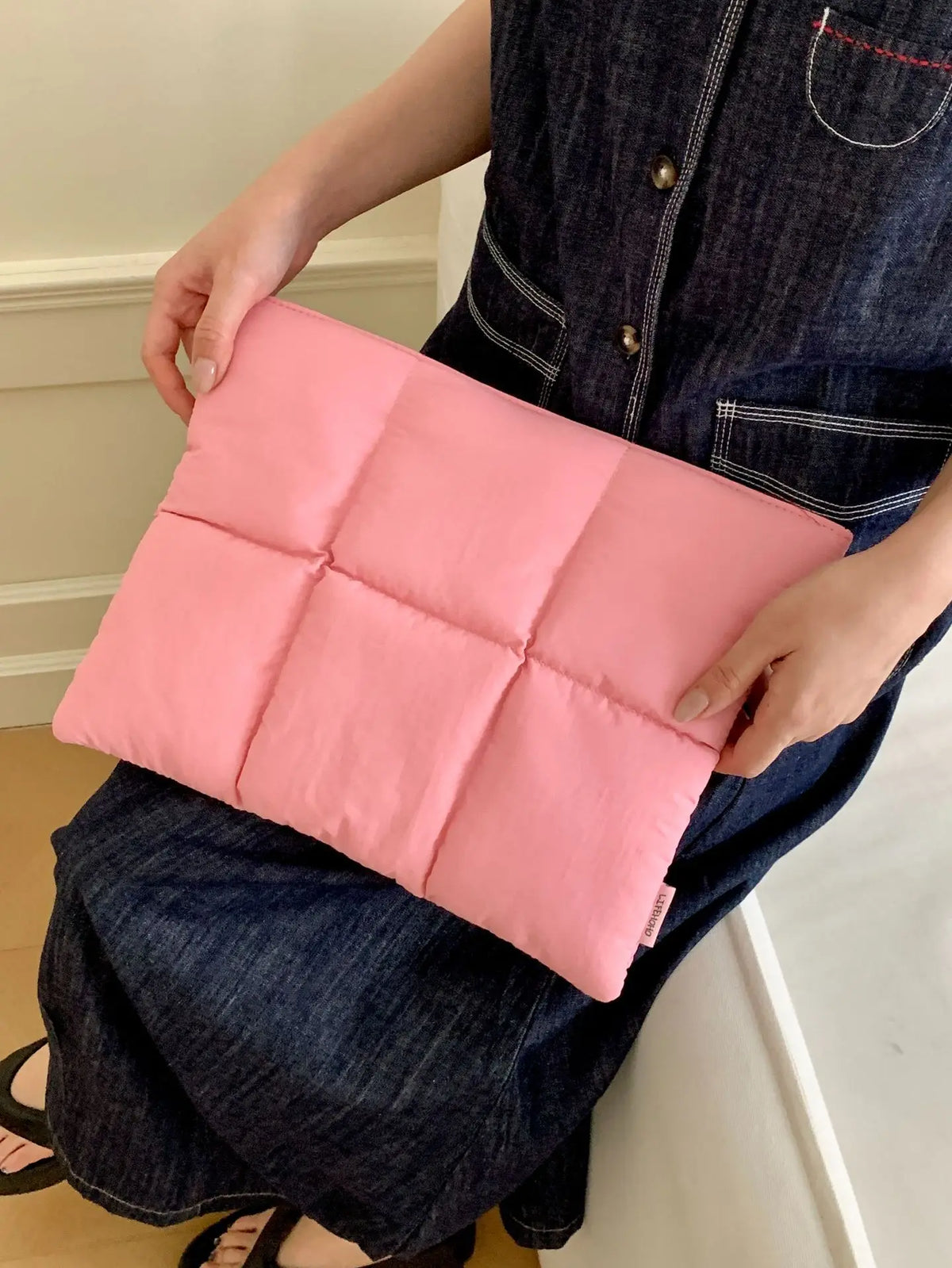 Pinke gesteppte Puffer-Laptoptasche mit Reißverschluss, gehalten von Person in dunklem Jeanshemd.