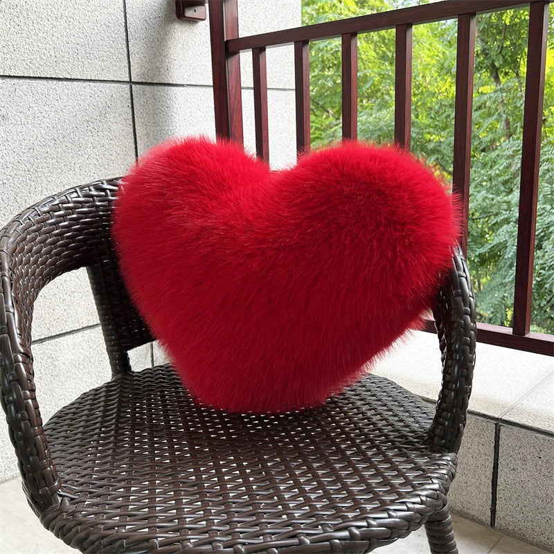 A bright red plush heart-shaped throw pillow resting on a dark brown wicker chair.