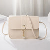 A beige compact crossbody handbag with a gold-tone chain charm and adjustable strap, shown on a white surface.