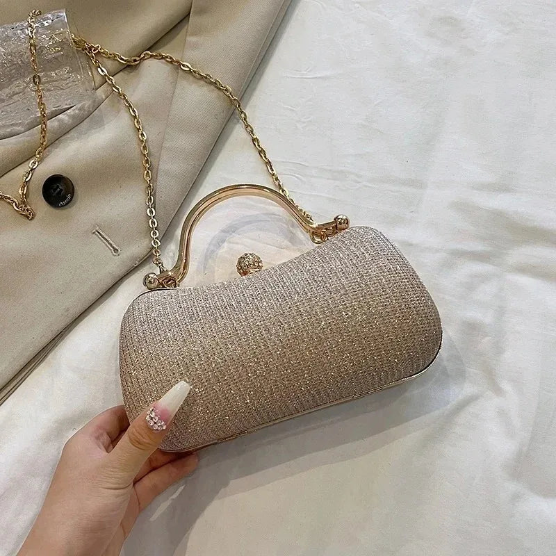 A hand holds a shimmering gold envelope clutch with a chain strap against a white background.