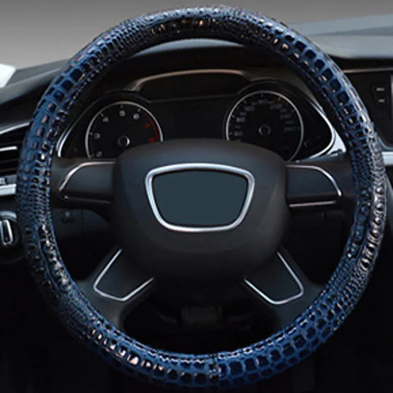 A close-up view of a black car steering wheel covered in blue crocodile grain leather.