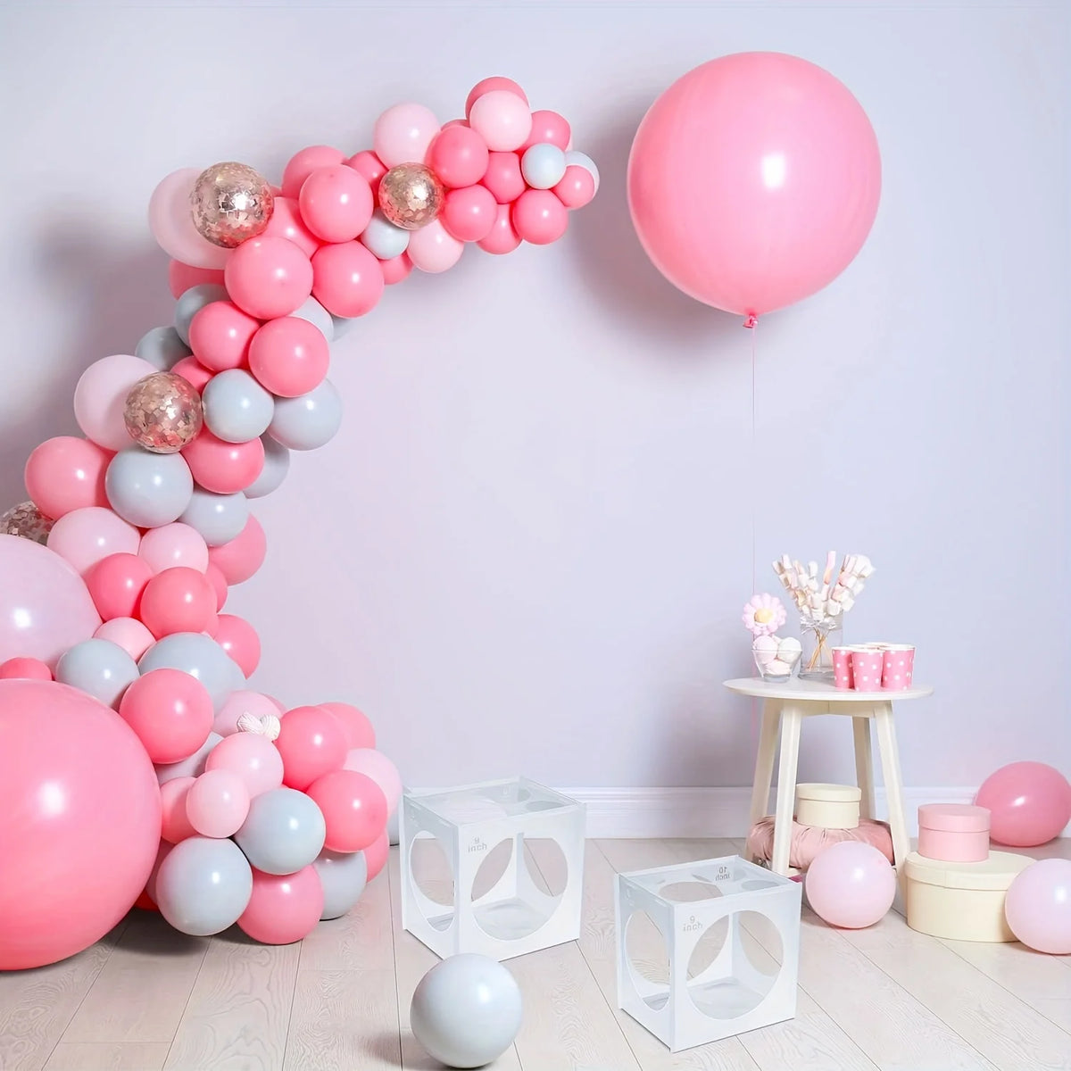 A display of pink and light blue balloons arranged in a curved wall decoration with a large pink balloon floating nearby.
