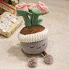 A cute artificial flower plush doll with pink roses and green leaves, sitting on a gray body with white trim.