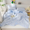 Light blue quilted blanket with a white floral pattern displayed on a bed.