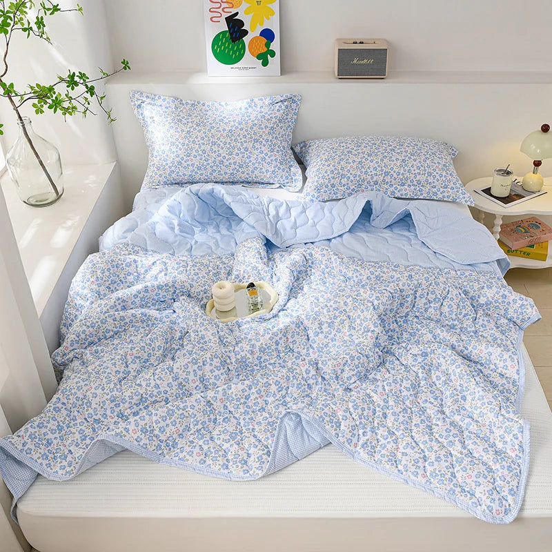 Light blue quilted blanket with a white floral pattern displayed on a bed.