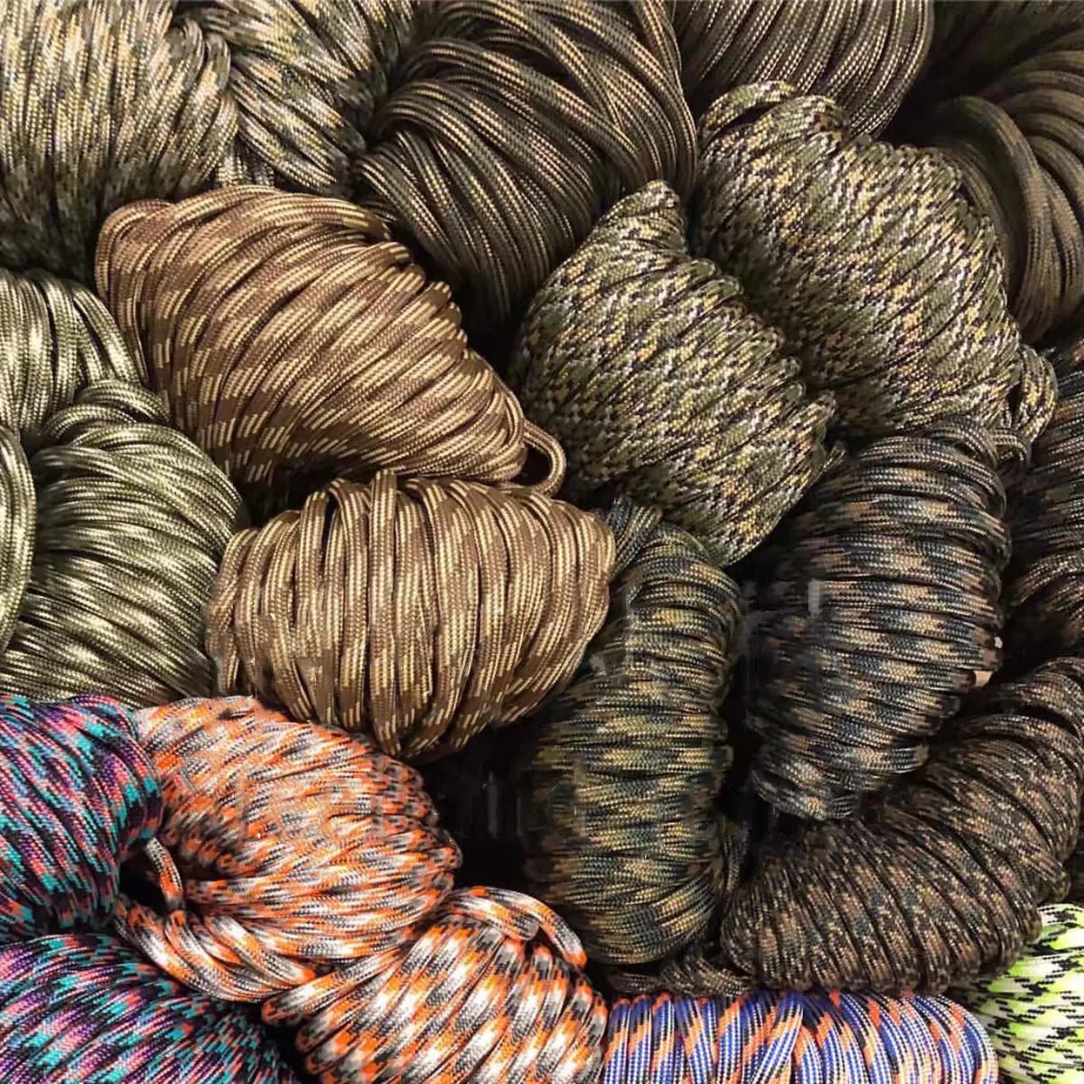 A close-up view of various spools of multi-purpose paracord rope in shades of brown, olive green, and dark gray.