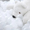 A white teddy bear toy is partially submerged in a large pile of clear plastic ball pit balls.