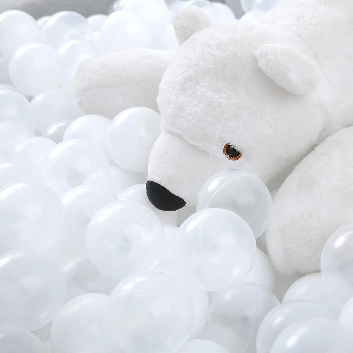A white teddy bear toy is partially submerged in a large pile of clear plastic ball pit balls.