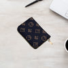 A dark patterned zippered card holder wallet resting on a light wooden surface next to a pen and a laptop.