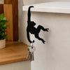 Black monkey-shaped wooden wall hook for keys and decor mounted on a white shelf.