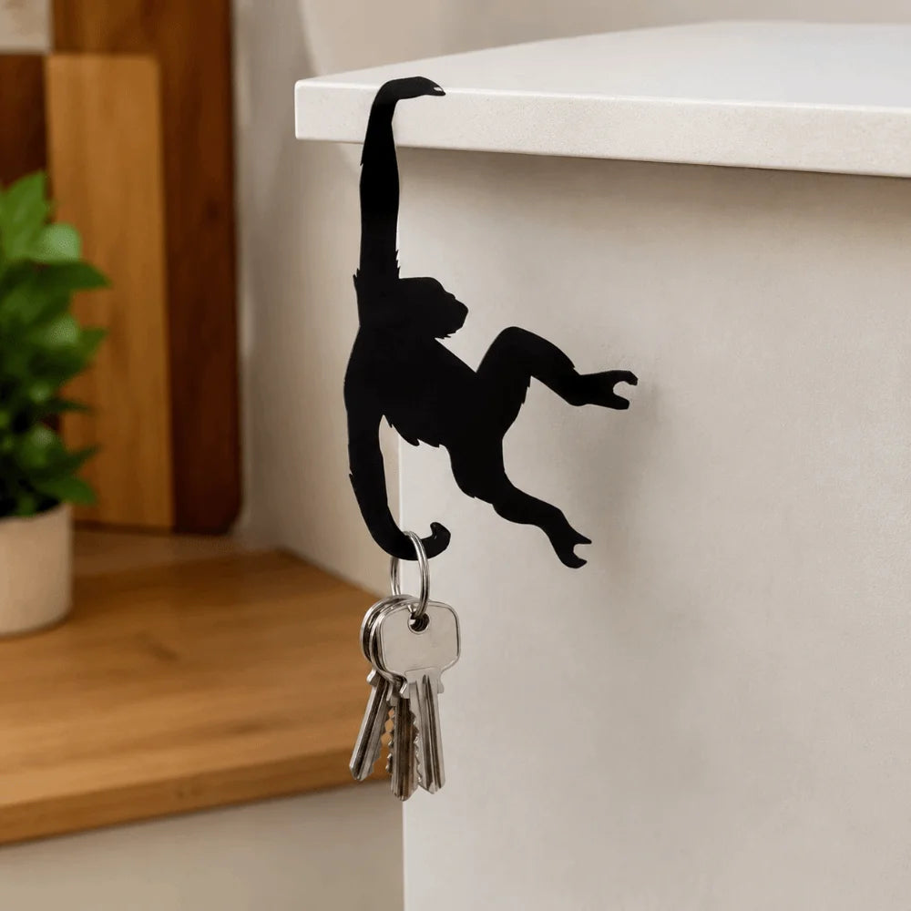 Black monkey-shaped wooden wall hook for keys and decor mounted on a white shelf.