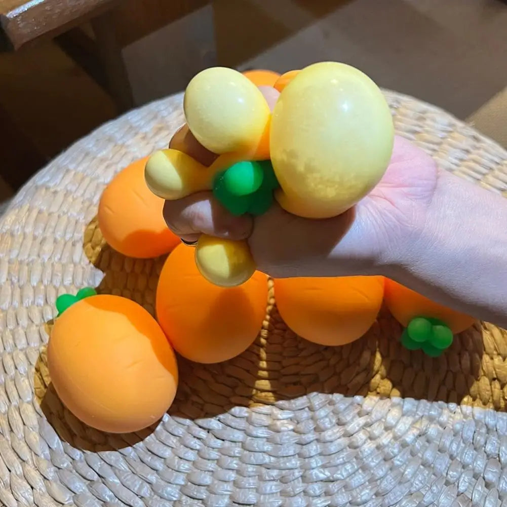 A hand holds several yellow and orange carrot-shaped squishy toys on a woven mat.