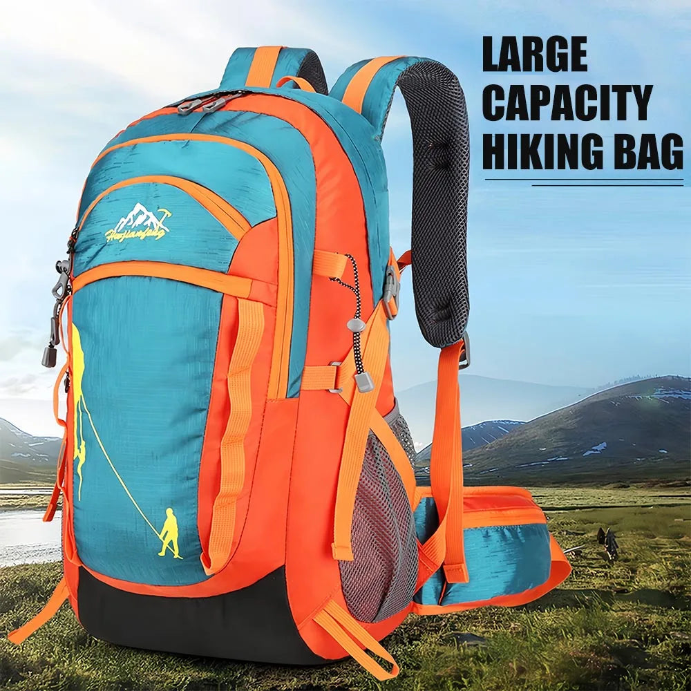 An orange and blue hiking backpack is shown outdoors on a grassy field with mountains in the background.